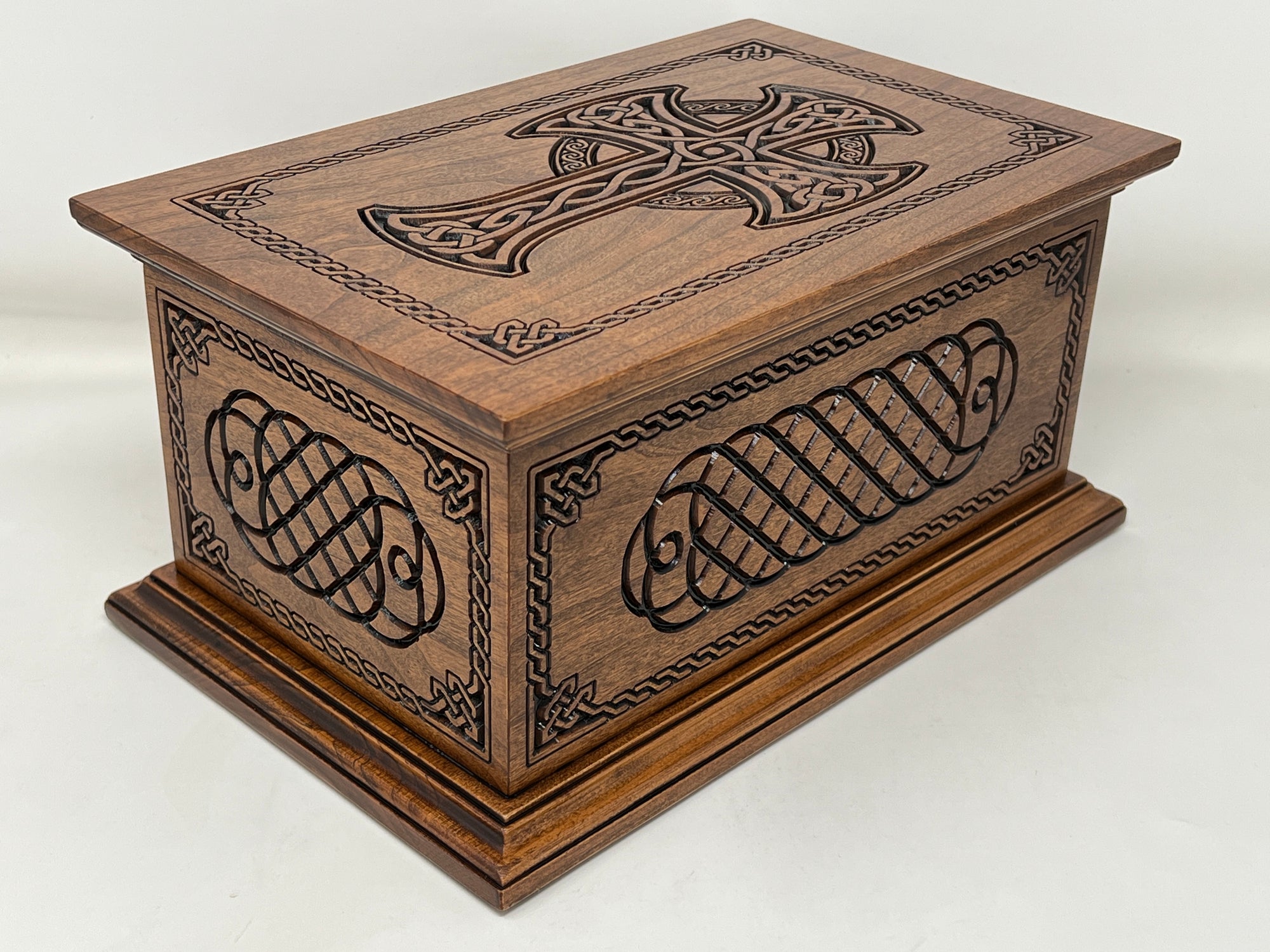 Image shows the top and two sides of the Celtic Cross and Weave Urn. The top has been carved with a woven celtic cross surrounded with a celtic boarder. The sides are carved with  celtic knot carvings and the same celtic boarder as the top. The endges of the top and bottom are nicely finished with moldings.