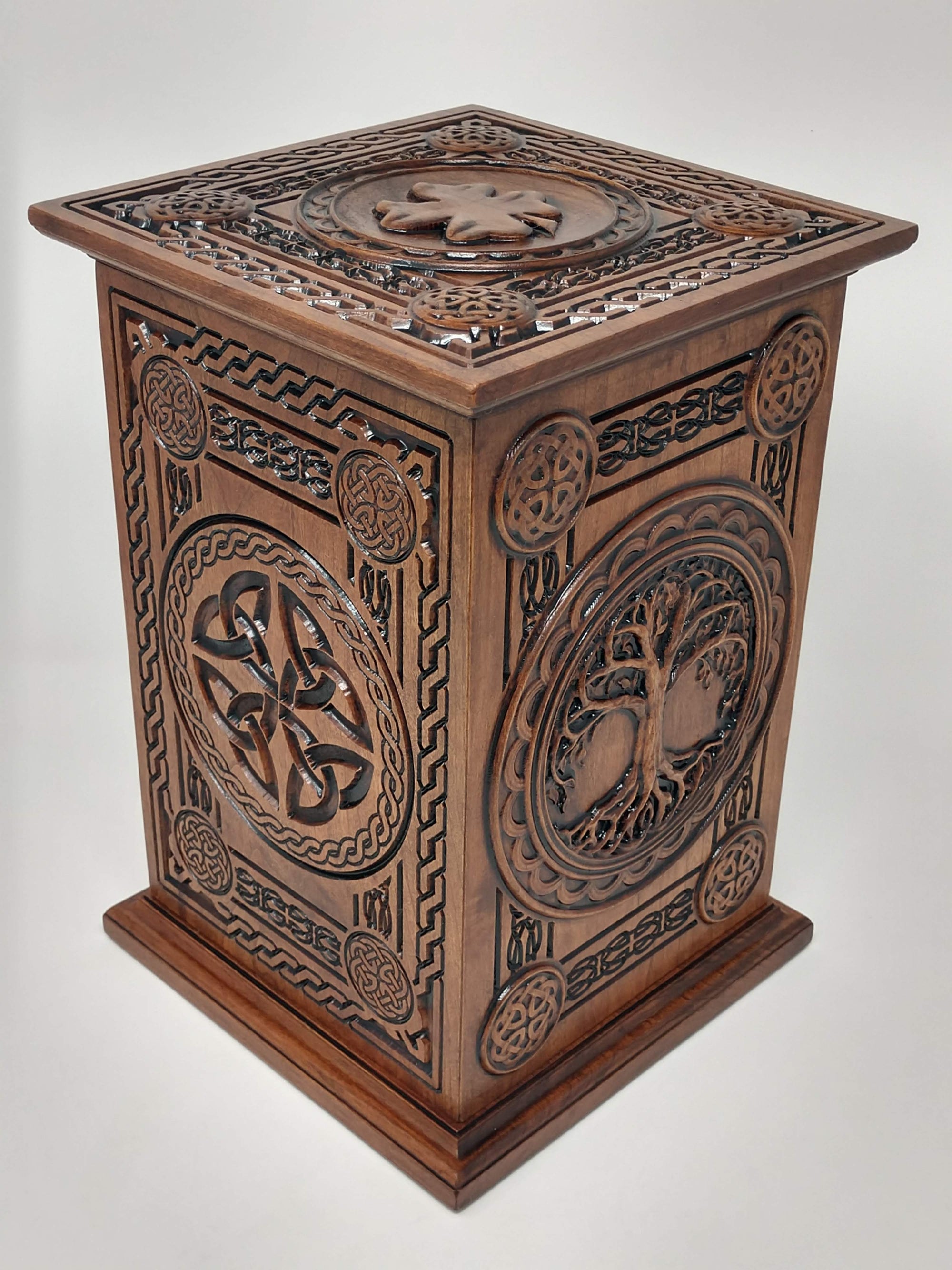 Images shows the urn from the left corner showing the left side with the Celtic Trinity knots and other celtic weaves and knot designs and boarders with the shamrock/four leaf clover caring on the top. The front with the Celtic Tree of Life us shown in this image of the ash urns for humans