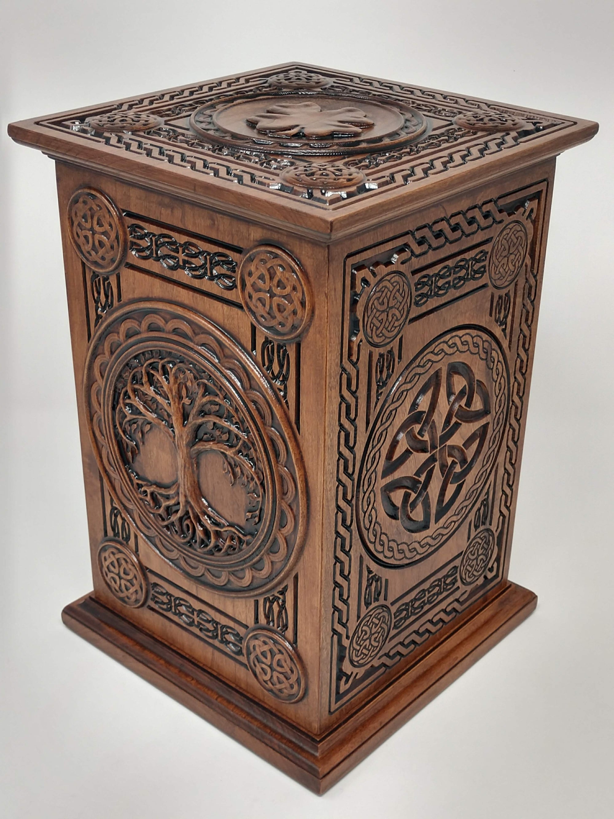 Ash urns for humans view from the right corner showing the right side with the Celtic Trinity knots and other celtic weaves and knot designs and boarders with the shamrock/four leaf clover caring on the top. The front with the Celtic Tree of Life us shown in this image of the ash urns for humans